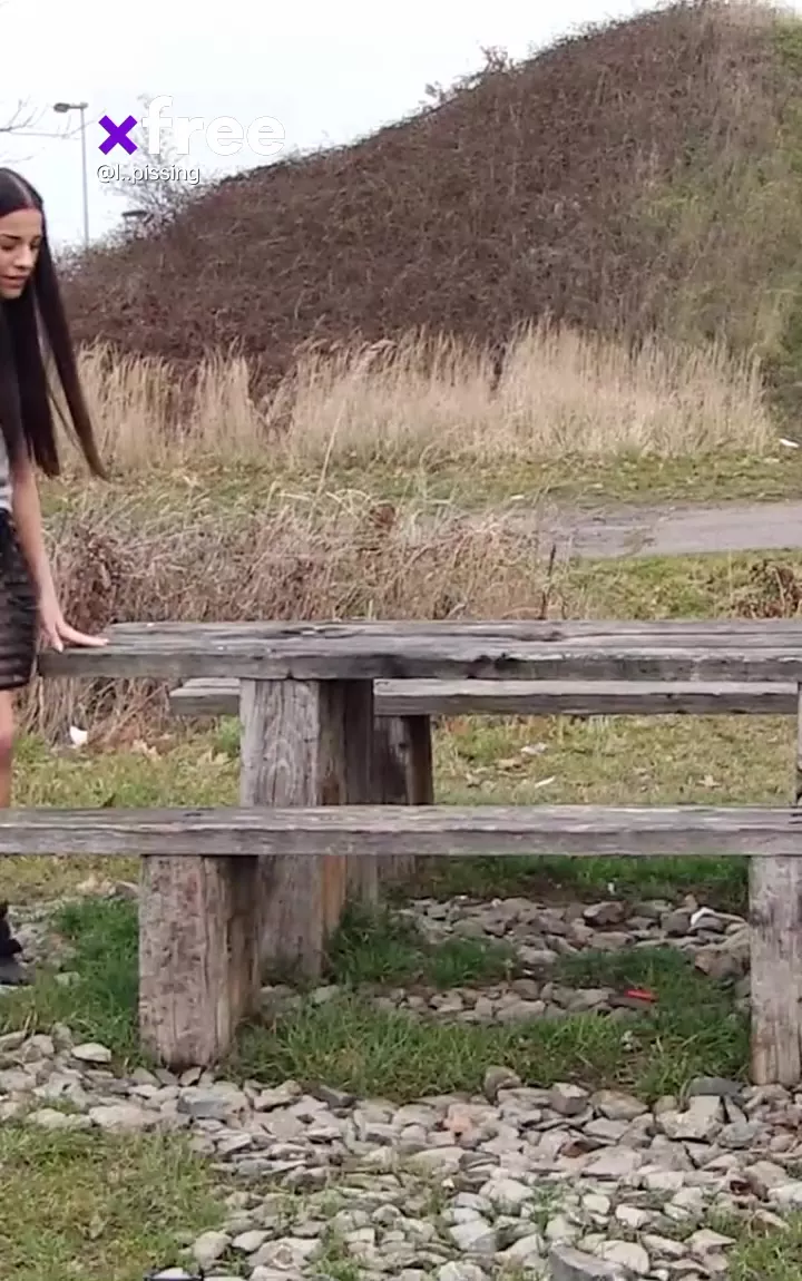 This feisty brunette is pissing outdoors while casually sitting on a bench,  like no fucking public